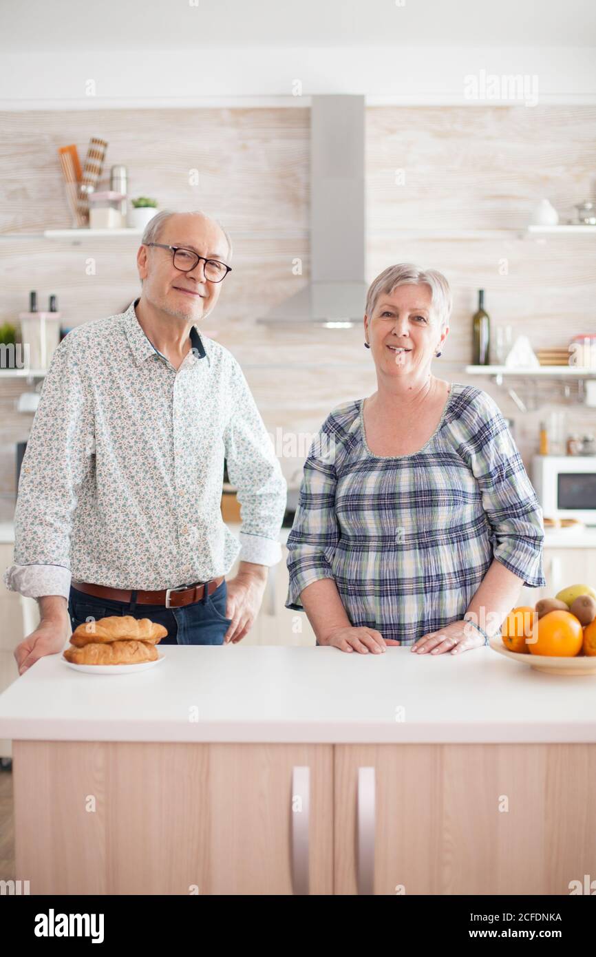 Portrait d'un couple senior souriant tout en regardant l'appareil photo dans la cuisine. Joyeux homme et femme souriant et riant. Heureux personnes âgées retraités dans la maison confortable appréciant la vie Banque D'Images