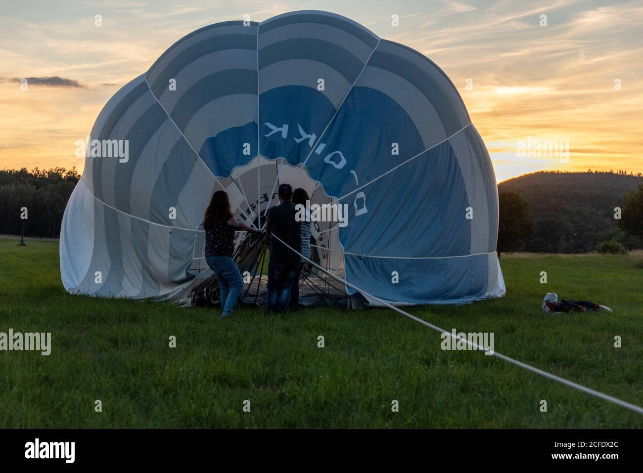Allemagne, Thuringe, Ellrich, trois personnes tirant une montgolfière, coucher de soleil. Banque D'Images