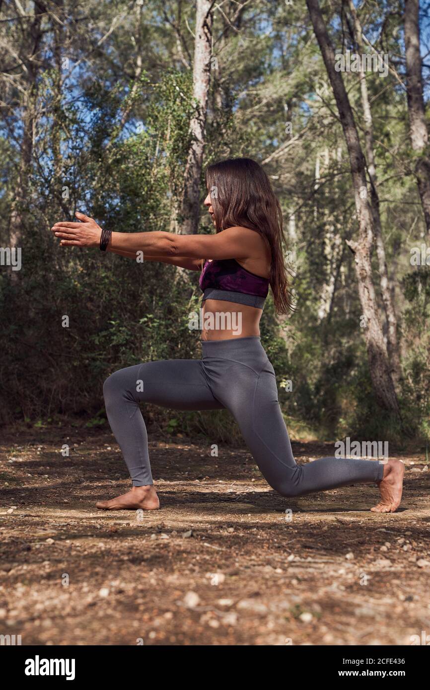 Corps complet de jeune femme en sport pratiquant la variation D'Anjaneyasana pendant le cours de yoga dans la forêt de printemps sur frais air Banque D'Images