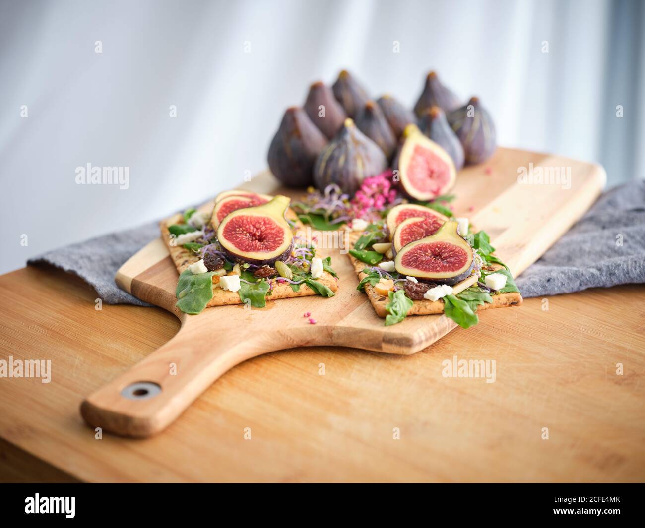 Délicieux sandwichs ouverts colorés faits maison avec des tranches de figues et morceaux de fromage sur du pain de seigle croustillant parmi le vert aromatique feuilles de roquette et fleurs roses Banque D'Images