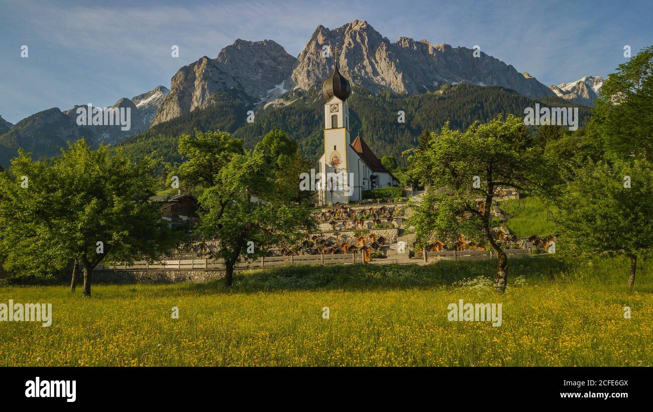 Église paroissiale de Saint-Jean-Baptiste à Grainau au printemps, vue vers Waxensteine dans les montagnes de Wetterstein, prairie verte, fleurs, arbres, bleu Banque D'Images