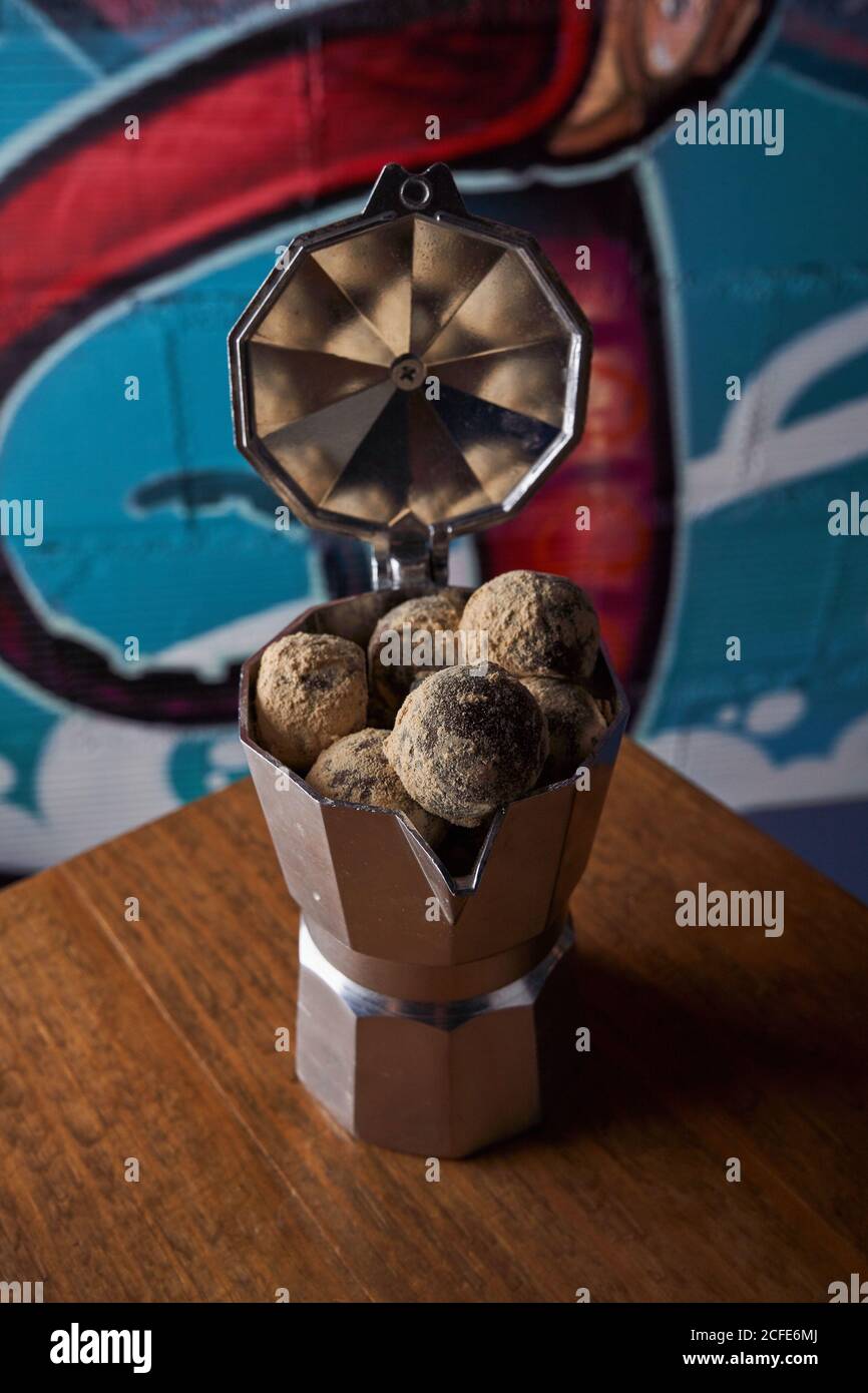 Depuis le dessus de la machine à café avec cuisinière en acier inoxydable et balles rondes de délicieuses truffes au chocolat servies à table contre le mur graffitis Banque D'Images