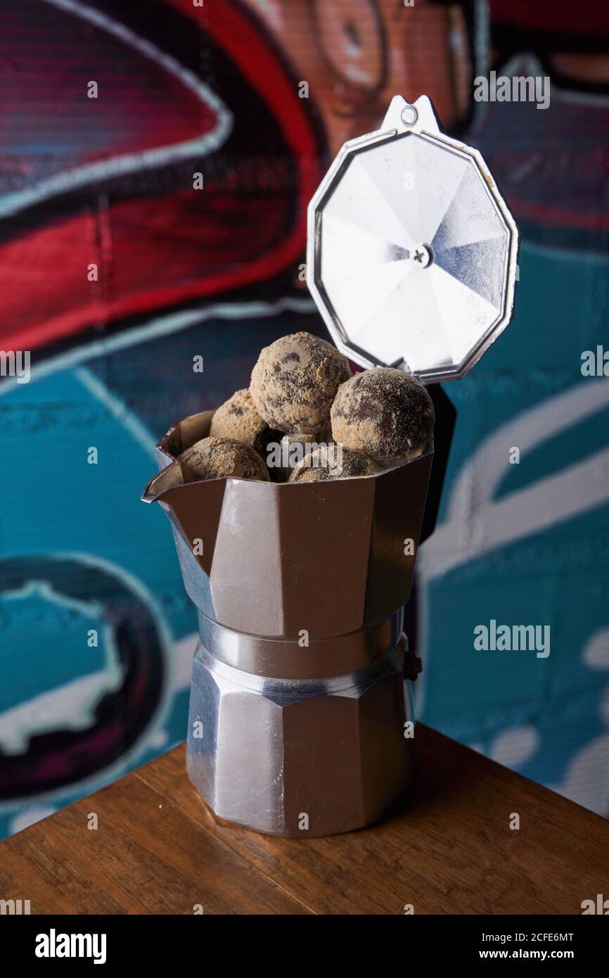 Depuis le dessus de la machine à café avec cuisinière en acier inoxydable et balles rondes de délicieuses truffes au chocolat servies à table contre le mur graffitis Banque D'Images