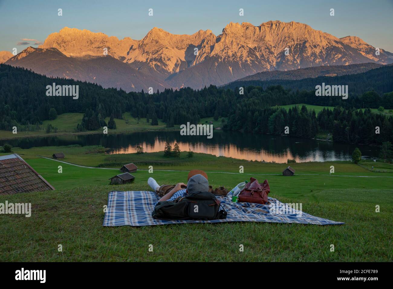 Le jeune homme en costume traditionnel se trouve sur une couverture de pique-nique près de Gerold contre les montagnes Karwendel, Geroldsee, postglow, promenade, poteau en bois, Banque D'Images