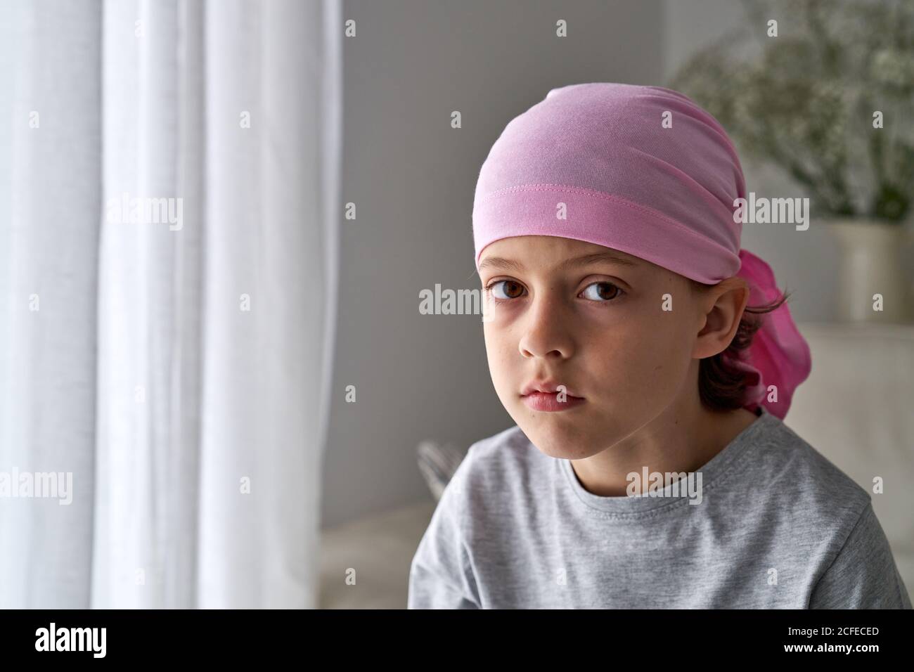 Sérieux mignon enfant dans le bandana rose regardant l'appareil photo et combattre le cancer chez soi Banque D'Images