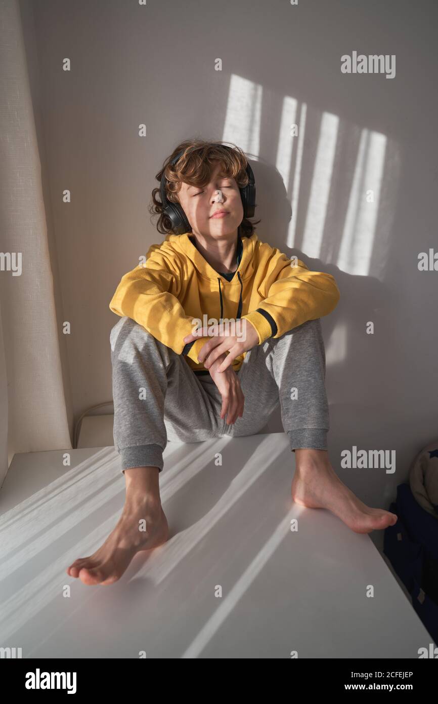 Un Enfant Heureux Dans Un Casque Un Chandail Jaune Et Un Pantalon Gris Asseyez Vous Les Yeux Fermes Et Ecoutez La Chanson Tout En Vous Relaxant Seul A La Maison Photo Stock