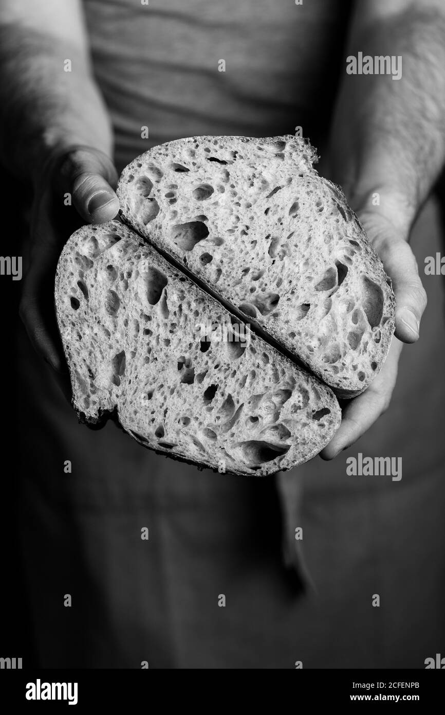 Crop mâle boulanger dans le tablier tenant coupé en demi-pain de pain frais et sain artisanal Banque D'Images