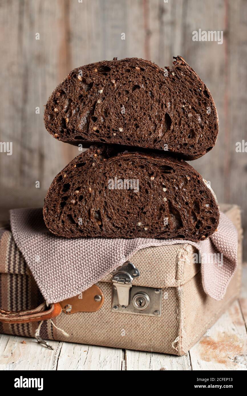 Appétissant pain de seigle noir sain avec des grains coupés la moitié est placée sur une valise en tissu rétro sur une table en bois Banque D'Images