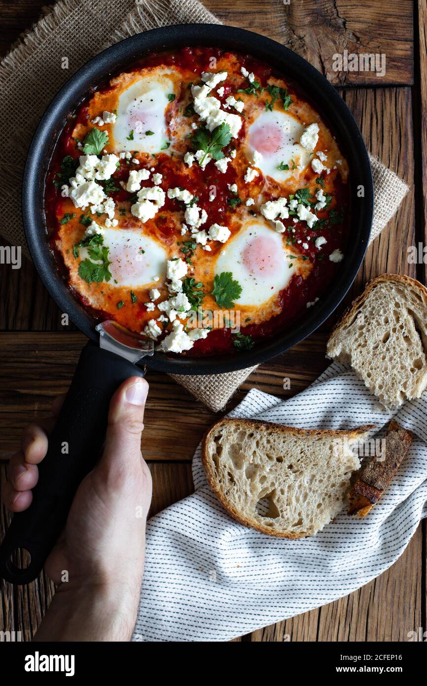 Vue de dessus d'un préposé à la récolte sur une table de cuisson en bois faites cuire avec de délicieux shakshuka préparés avec des œufs frits et des légumes et fromage feta Banque D'Images