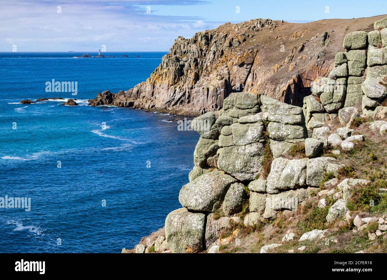 Vue détaillée sur les falaises de granit des Coves de Pendower avec une falaise plus élevée de Bosistow, un sentier côtier et un phare de Longships éloigné; côte de Cornouailles près de Lands End. Banque D'Images