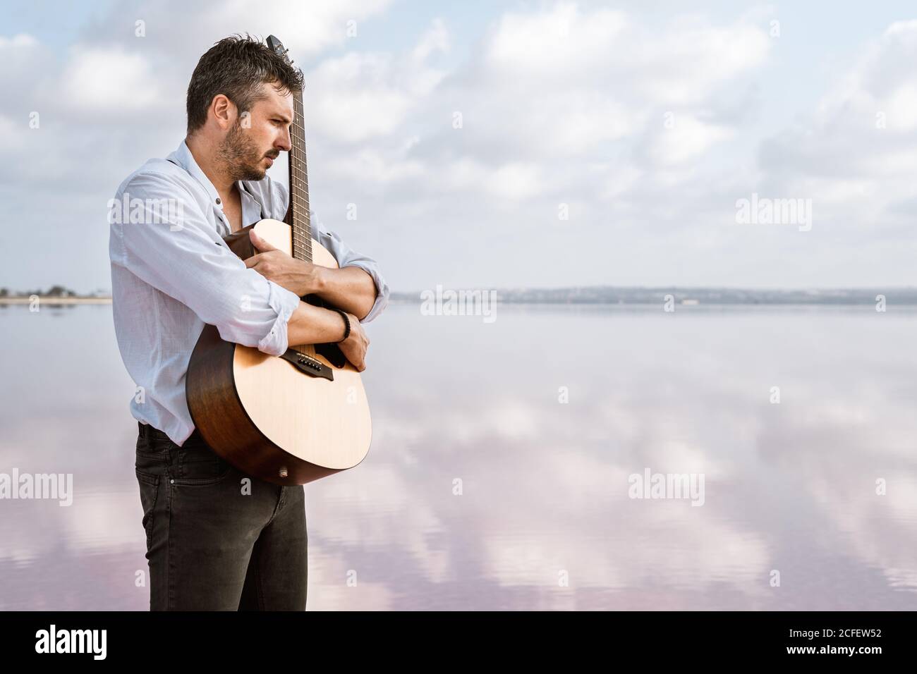 Homme passionné mélancholique en chemise blanche et bretelles embrassant la  guitare tout en vous tenant pieds nus dans l'eau par terre par jour nuageux  Photo Stock - Alamy