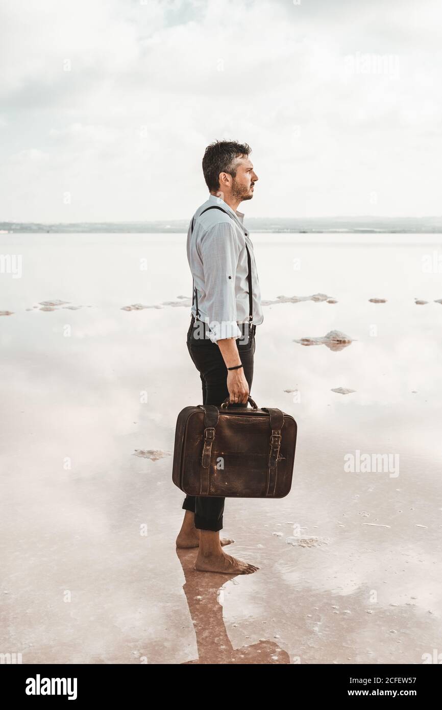 Vue latérale d'un homme en chemise blanche et bretelles de transport  Porte-documents miteux tout en se tenant pieds nus sur une plage sombre aux  États-Unis Photo Stock - Alamy