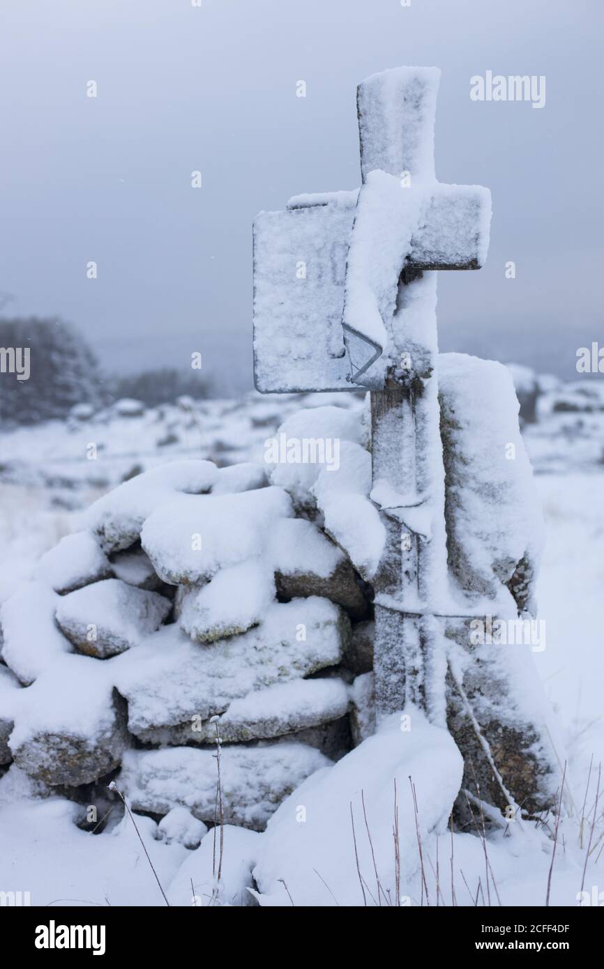 Croix en bois enneigée près des rochers avec champ vide neigeux et ciel gris nuageux sur fond Banque D'Images