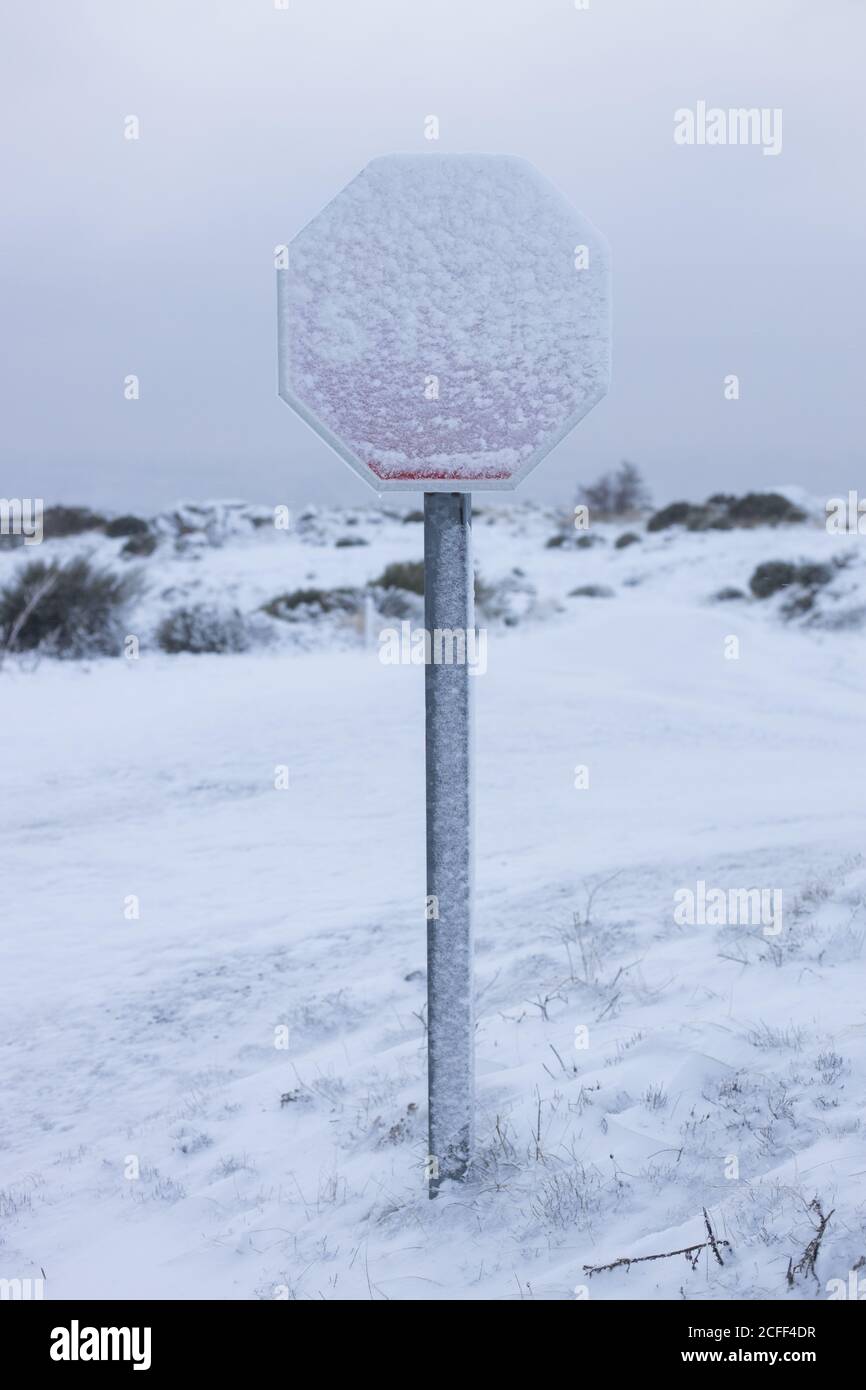 Panneau Snow Covered Stop sur terrain blanc et isolé de la colline contre le ciel gris sombre Banque D'Images