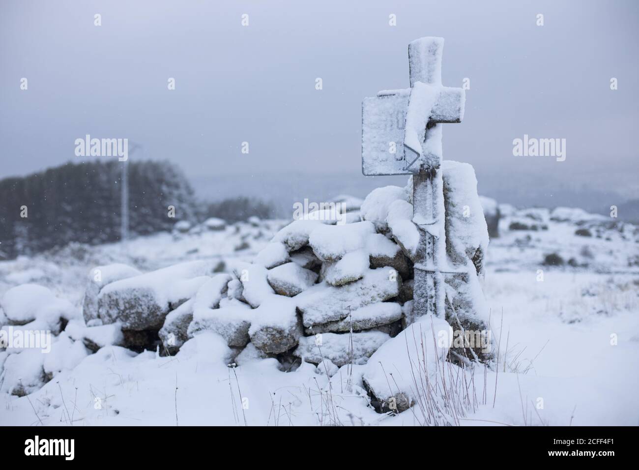 Croix en bois enneigée près des rochers avec champ vide neigeux et ciel gris nuageux sur fond Banque D'Images