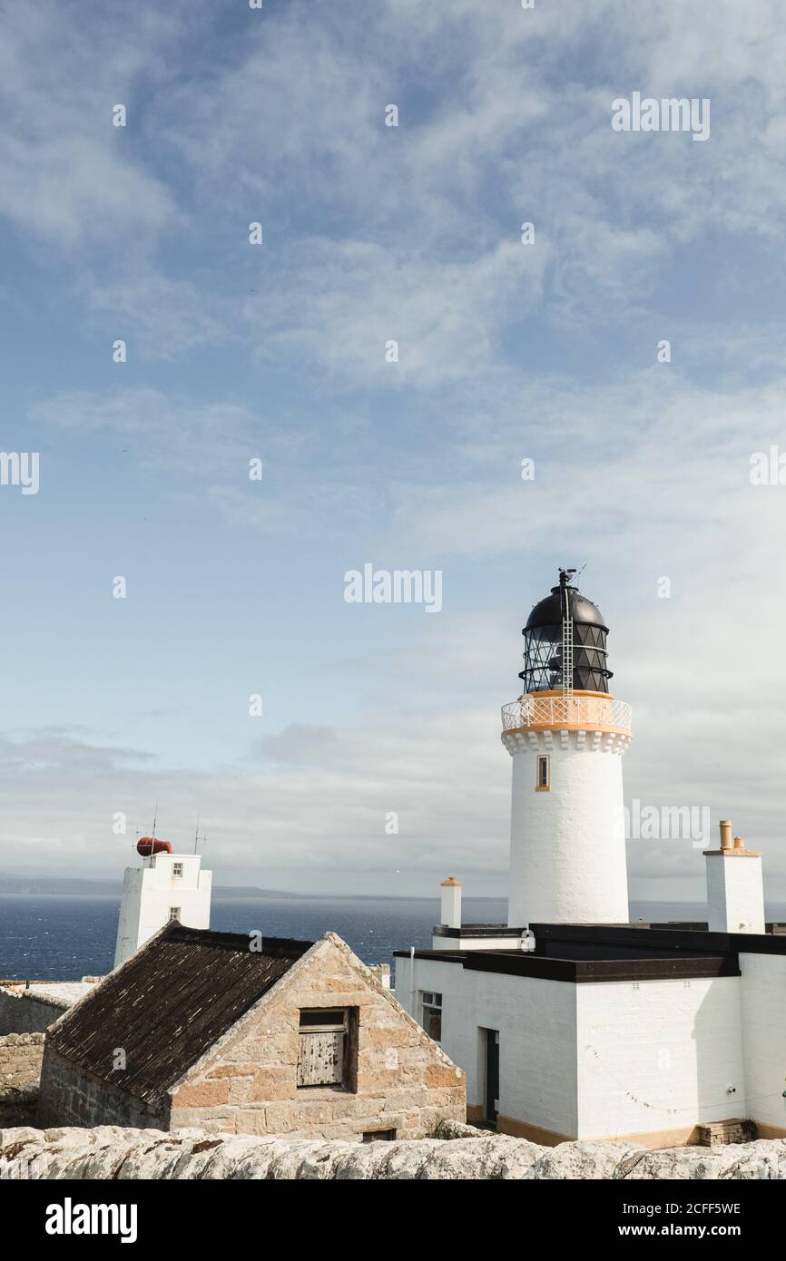 Magnifique phare blanc Dunnet Head dans les montagnes écossaises avec du bleu ciel et nuages blancs en arrière-plan Banque D'Images
