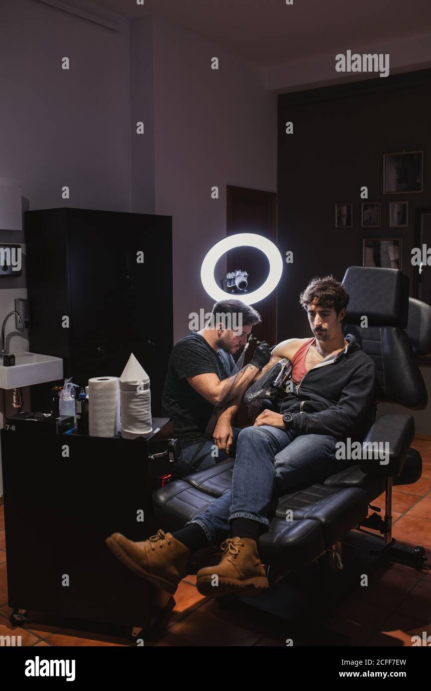 Maître faisant tatouage sur l'avant-bras du client mâle Banque D'Images