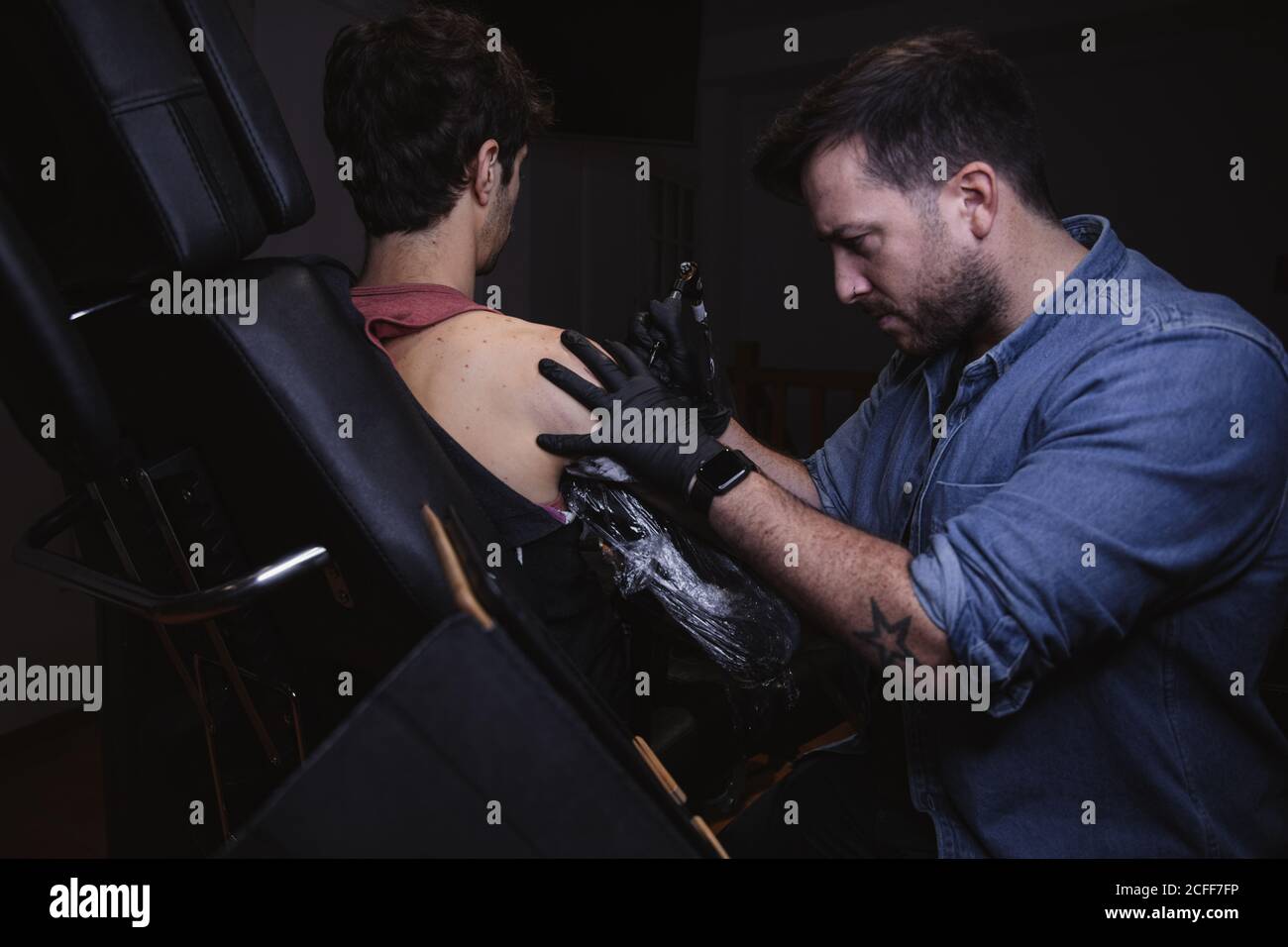 Maître faisant tatouage sur l'avant-bras du client mâle Banque D'Images