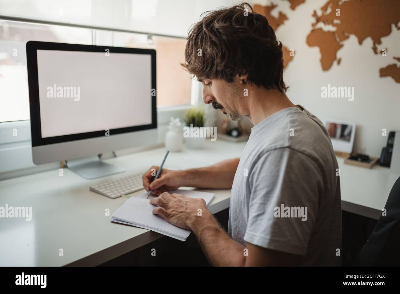 Vue latérale de l'homme entrepreneur prenant des notes dans le bloc-notes pendant travailler à distance à la maison Banque D'Images