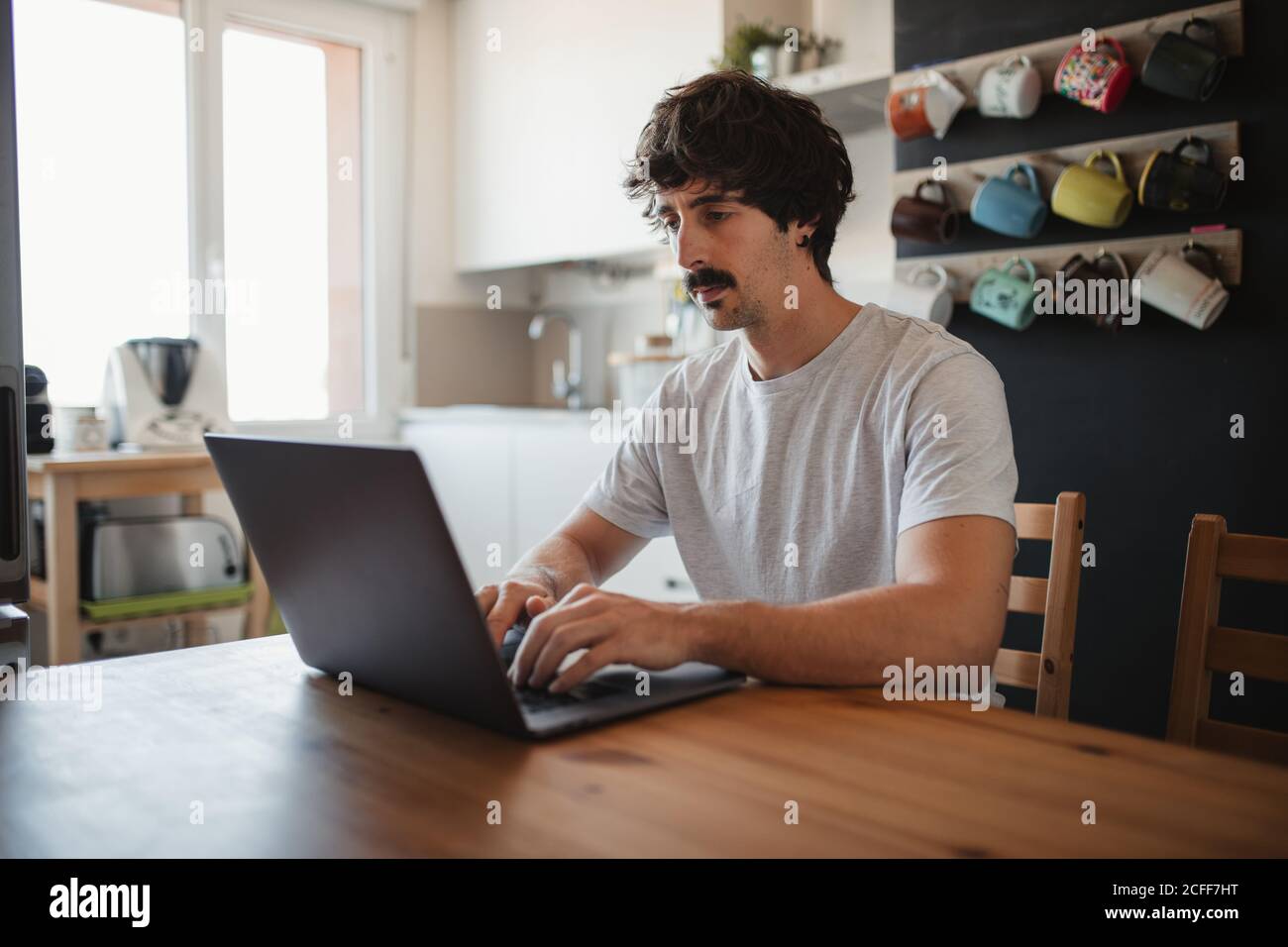 Vue latérale indépendante masculine, assise à une table dans la cuisine et travailler sur le projet en utilisant l'ordinateur Banque D'Images