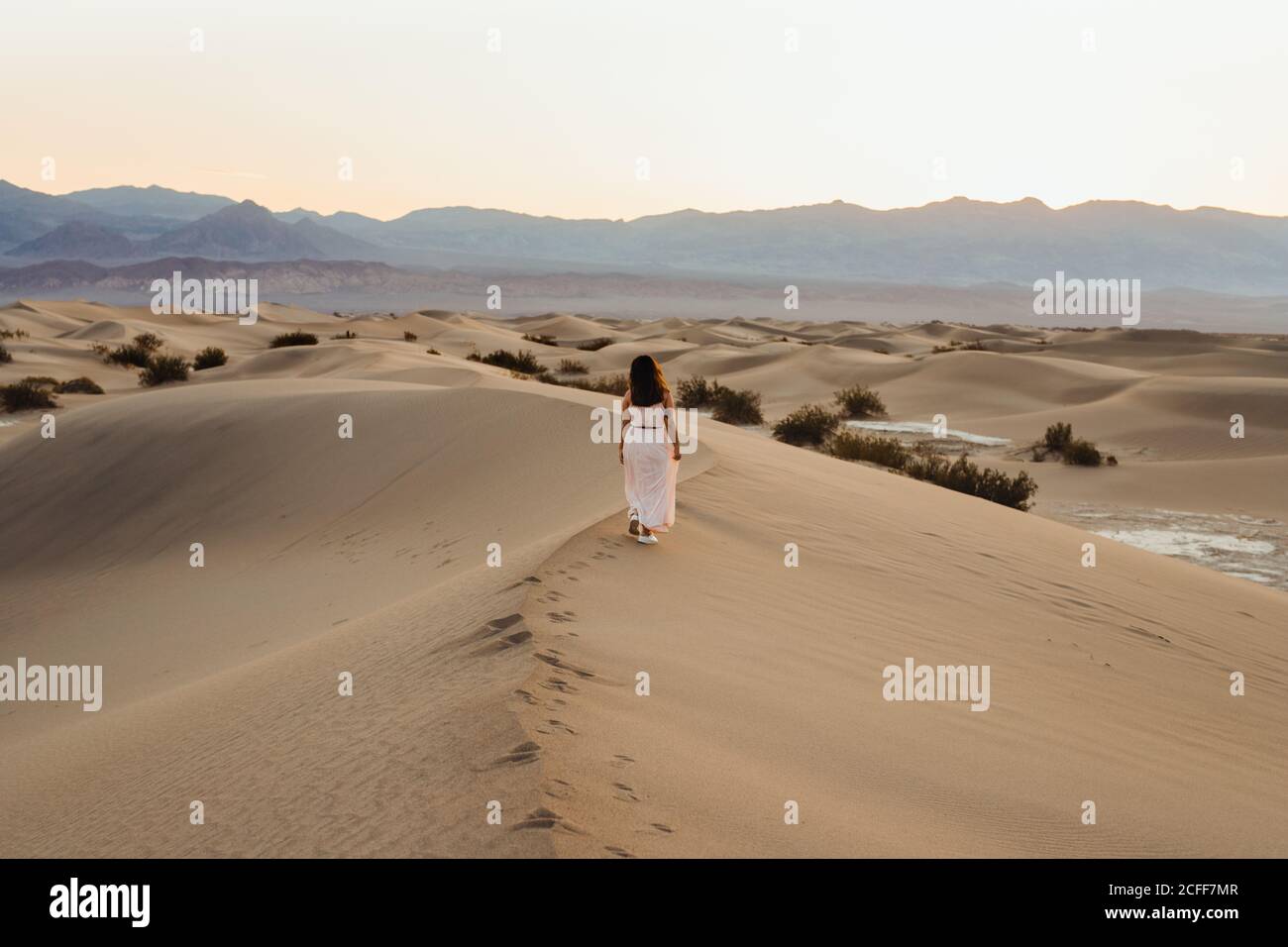 Vue arrière de la jeune femme marchant dans le désert laissant des empreintes de pas dans les dunes de sable sec de la vallée de la mort Banque D'Images