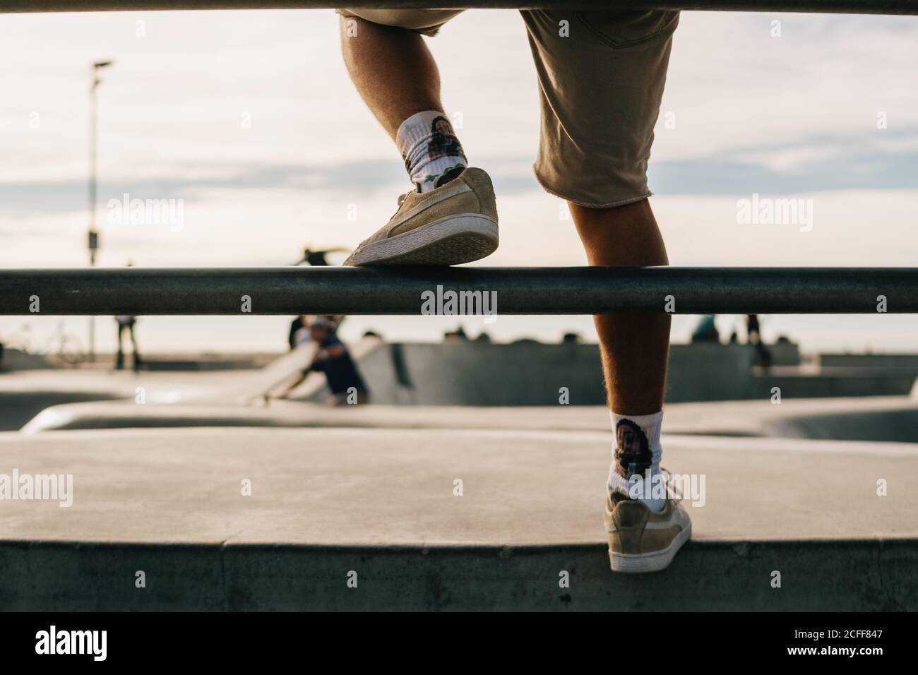 Venice Beach, États-Unis - 11 décembre 2017 : vue arrière d'un petit-homme en baskets assis sur une clôture en métal et en appréciant les patineurs sur la piste dans le parc Banque D'Images