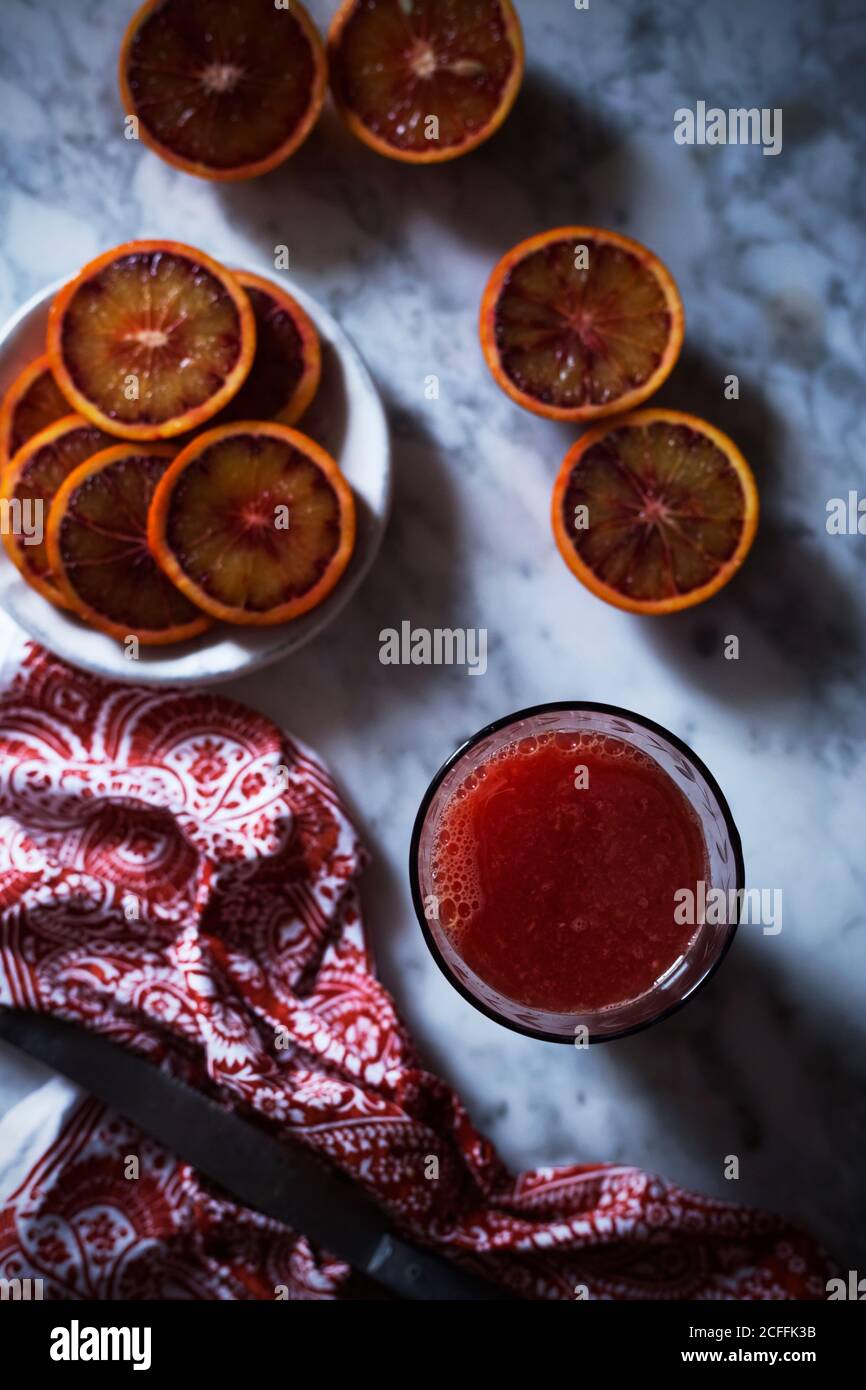 Du dessus du verre de boisson rouge placé près des tranches de orange de sang et serviette de table en marbre Banque D'Images