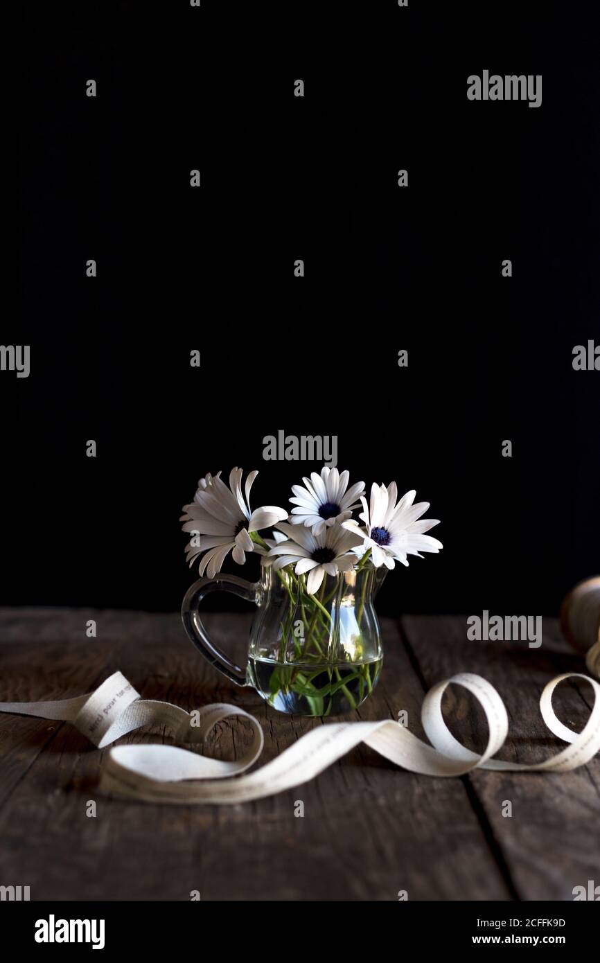 Ruban d'enroulement placé sur le plan d'examen en bois près du vase en verre avec fleurs blanches sur fond noir Banque D'Images