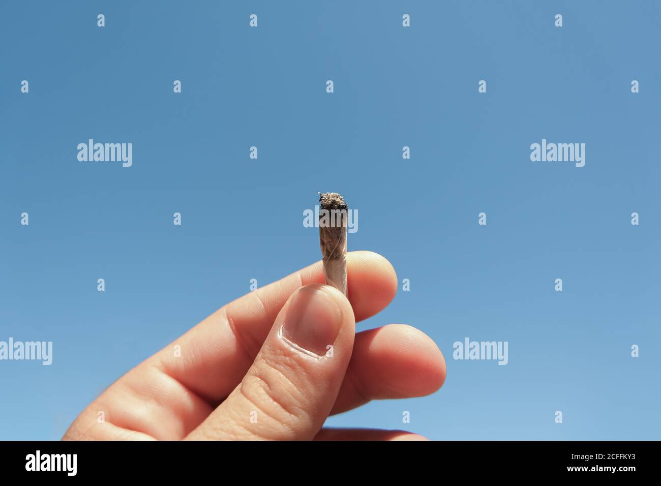 Main humaine tenir une cigarette de cannabis sur le ciel bleu contexte,tabagisme maladie de dépendance Banque D'Images