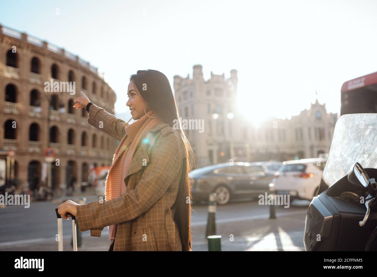 Vue latérale d'une femme asiatique avec une valise souriante et étirée en taxi dans la rue de la ville touristique Banque D'Images