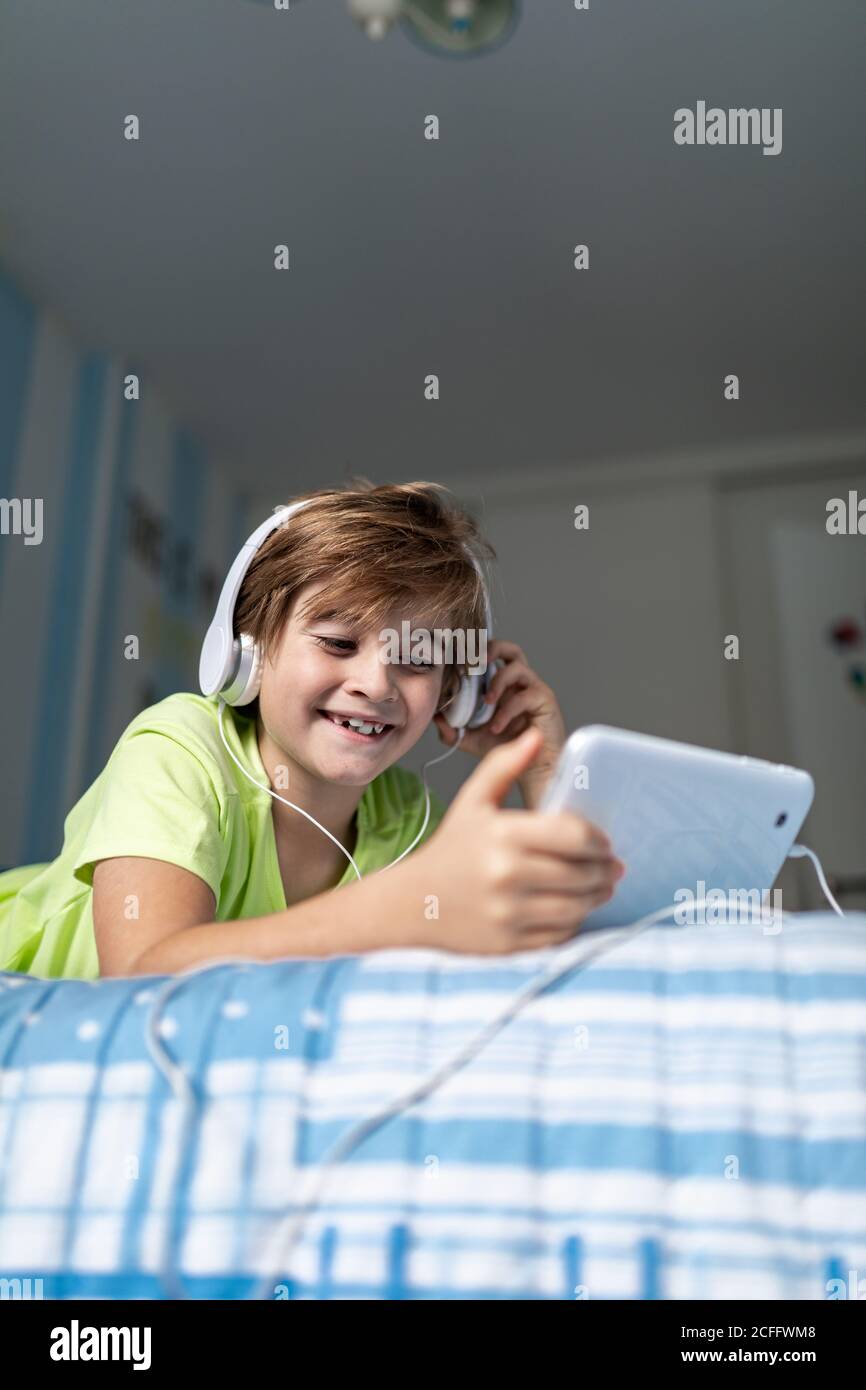 Préadolescents positifs, vêtements décontractés, avec écouteurs couchés se coucher et regarder un film sur une tablette tout en vous reposant à la maison Banque D'Images
