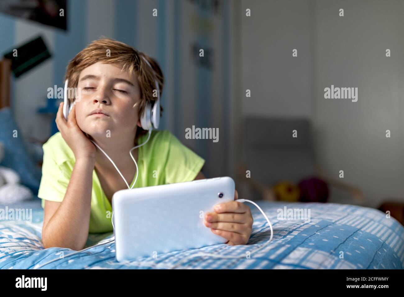 Préadolescents positifs, vêtements décontractés, avec écouteurs couchés se coucher et regarder un film sur une tablette tout en vous reposant à la maison Banque D'Images