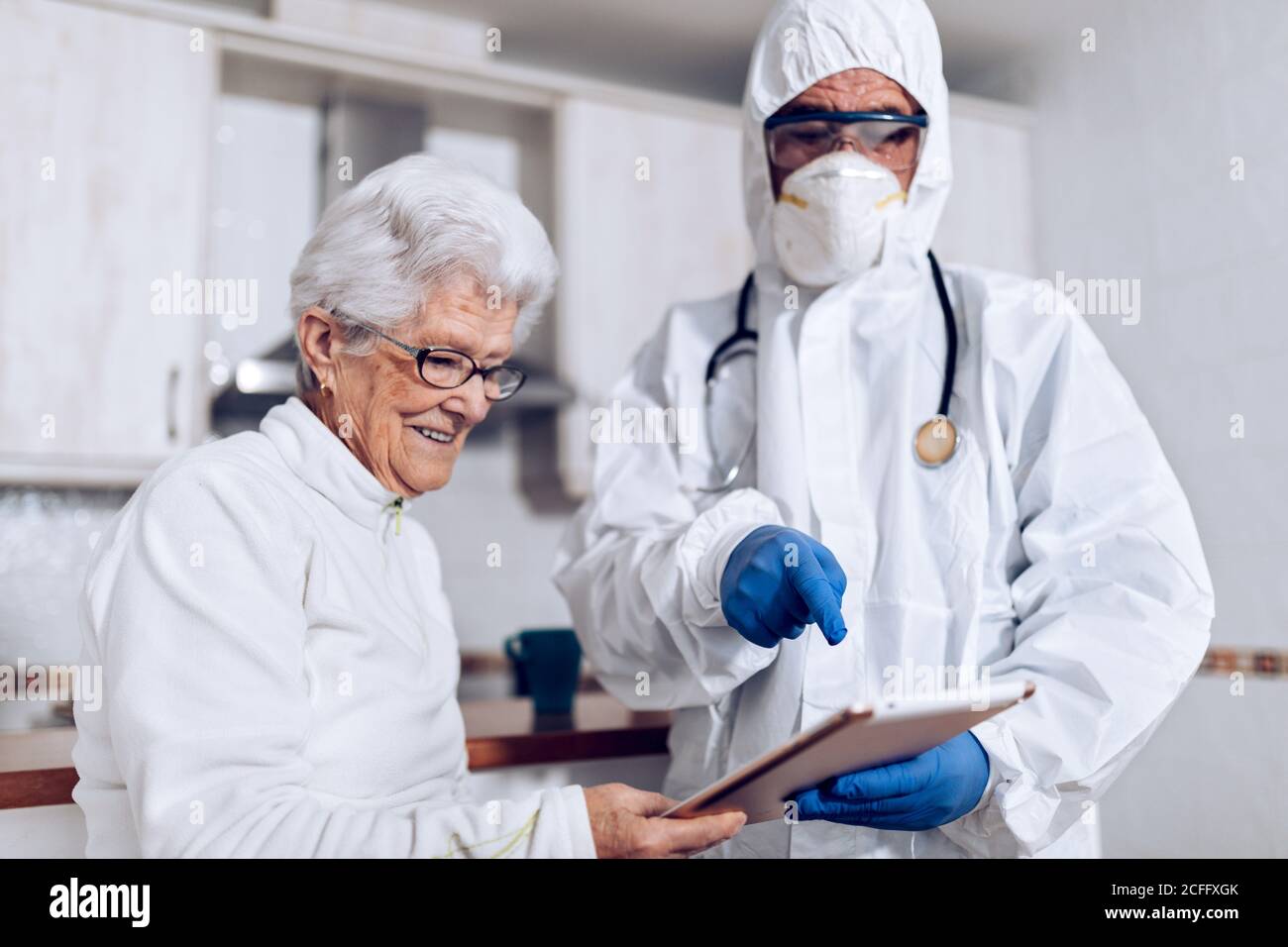 Homme non reconnaissable médecin spécialiste en costume de protection avec masque et gants rendant visite à une patiente âgée à la maison pendant le verrouillage du coronavirus et expliquer la prescription Banque D'Images