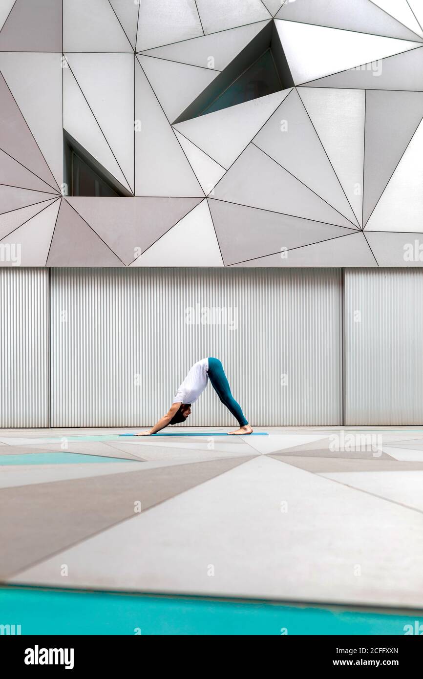 Vue latérale d'un homme adulte dans les vêtements de sport faisant face vers le bas Exercice de chien tout en faisant le yoga contre le mur géométrique dans spacieux chambre Banque D'Images