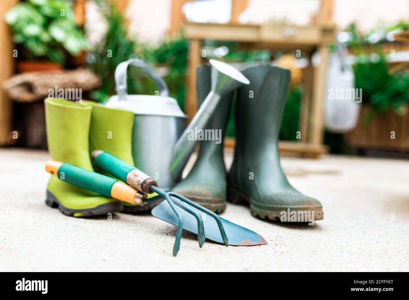 Outils de jardinage placés sur le sol près des bottes en caoutchouc et de l'arrosage can en serre Banque D'Images