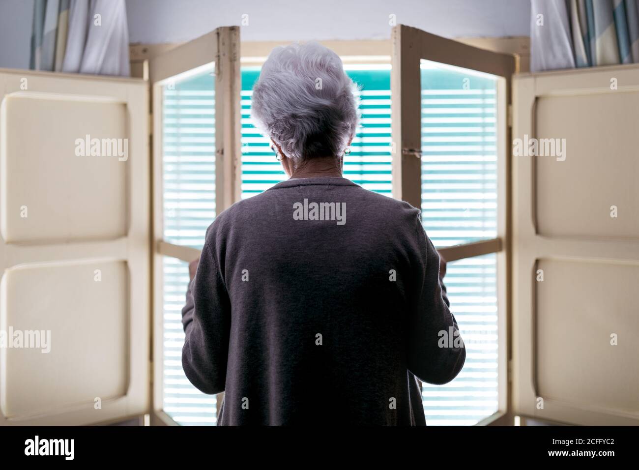 Femme aux cheveux gris debout devant la fenêtre à la maison Banque D'Images
