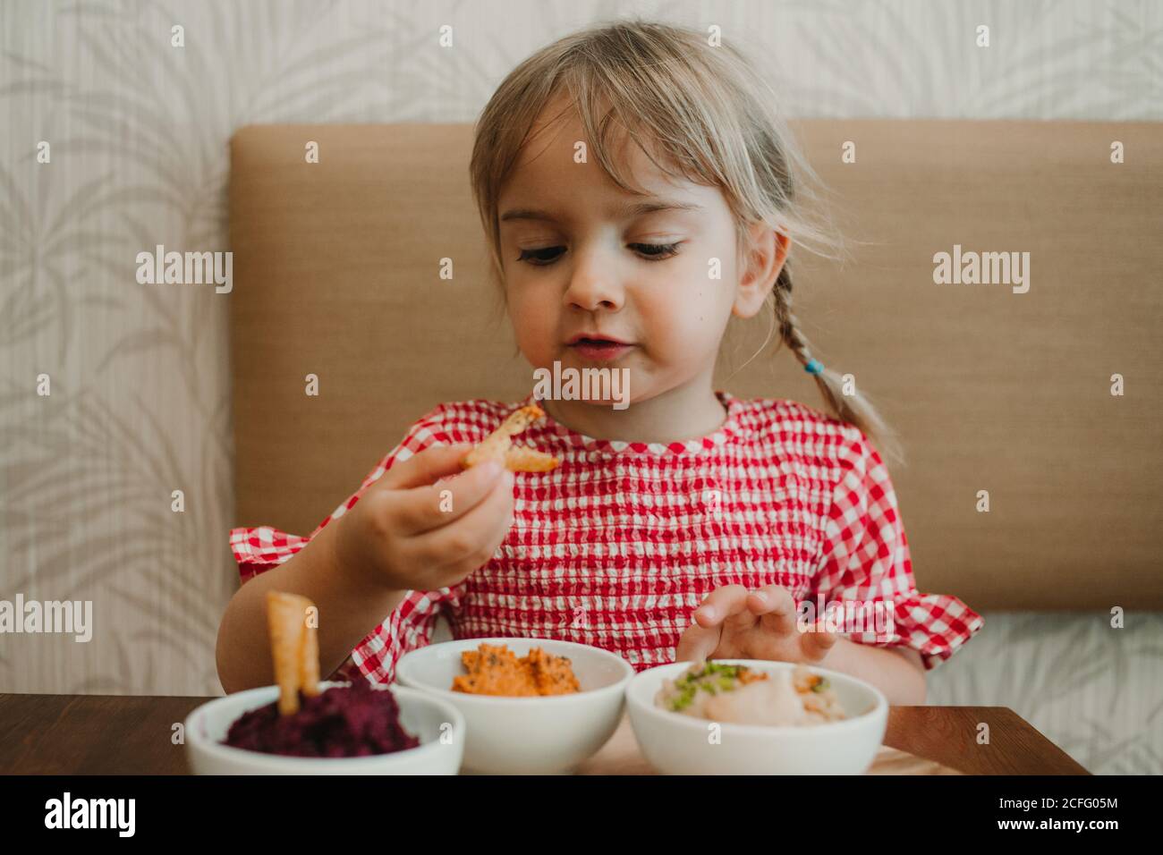 Petite fille mignonne mangeant des en-cas appétissants variés à table Banque D'Images