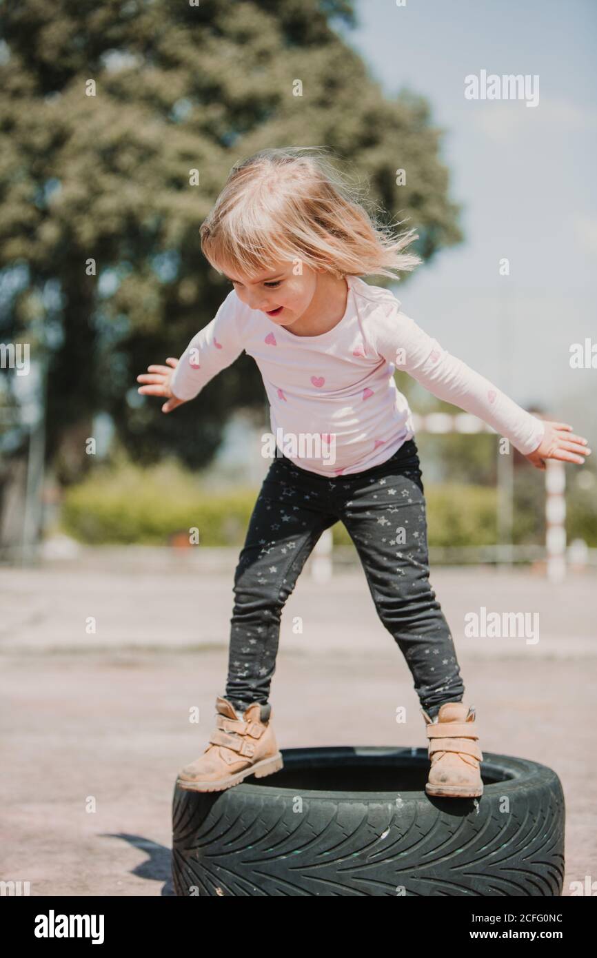 Bonne joyeuse petite fille ayant le plaisir et l'équilibre sur le noir pneus de voiture en jouant à l'extérieur le jour de l'été Banque D'Images