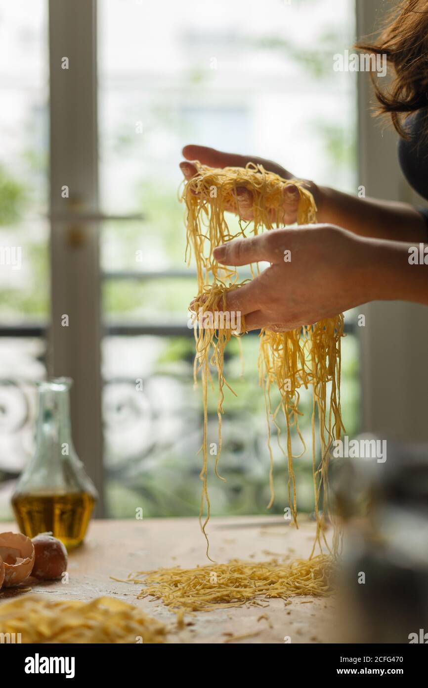 Femme tenant couper fines bandes de pâtes dans les mains pendant préparation du repas dans la cuisine Banque D'Images