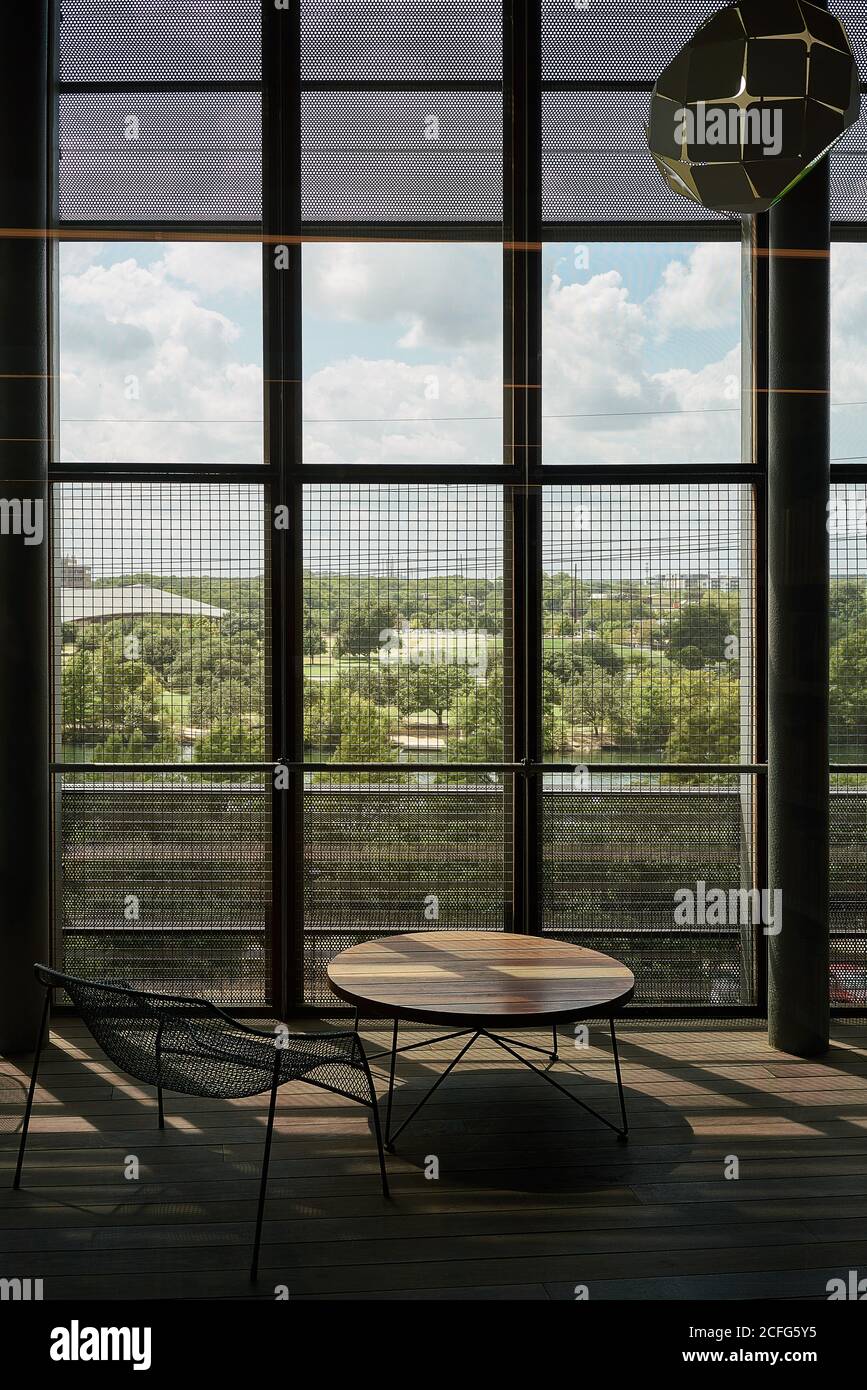 Coin salon avec table ronde en bois et chaise en métal contre De grandes fenêtres avec grille en lumière contrastée dans la bibliothèque du Texas Banque D'Images