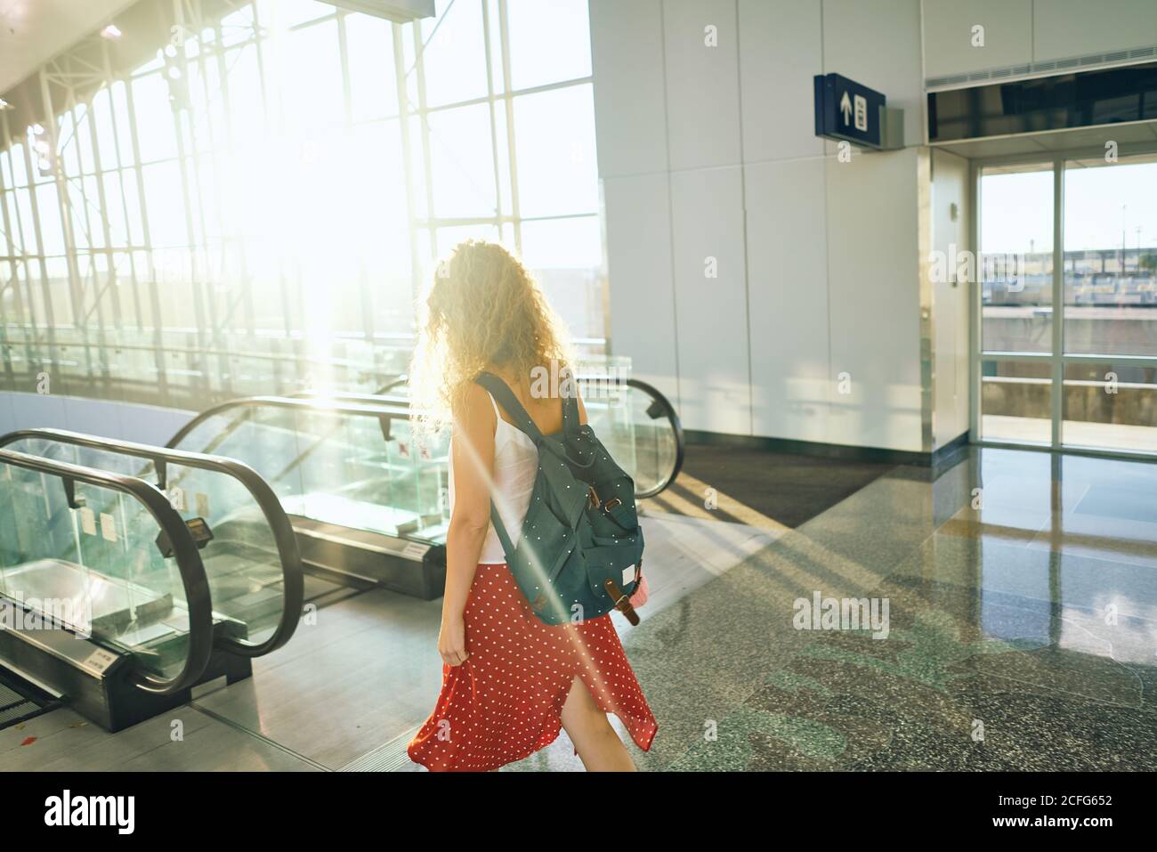 Vue latérale d'une charmante femme maurique en jupe rouge avec sac à dos à pied à l'escalier mécanique de l'aéroport au Texas Banque D'Images