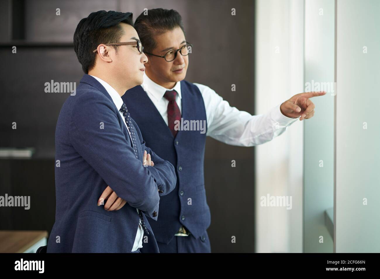 deux dirigeants d'entreprises asiatiques debout sous les fenêtres qui parlent au bureau Banque D'Images