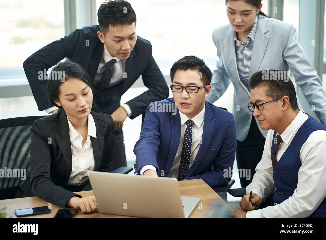 une équipe de cinq dirigeants d'entreprise asiatiques se réunit au bureau pour discuter les entreprises utilisant un ordinateur portable Banque D'Images