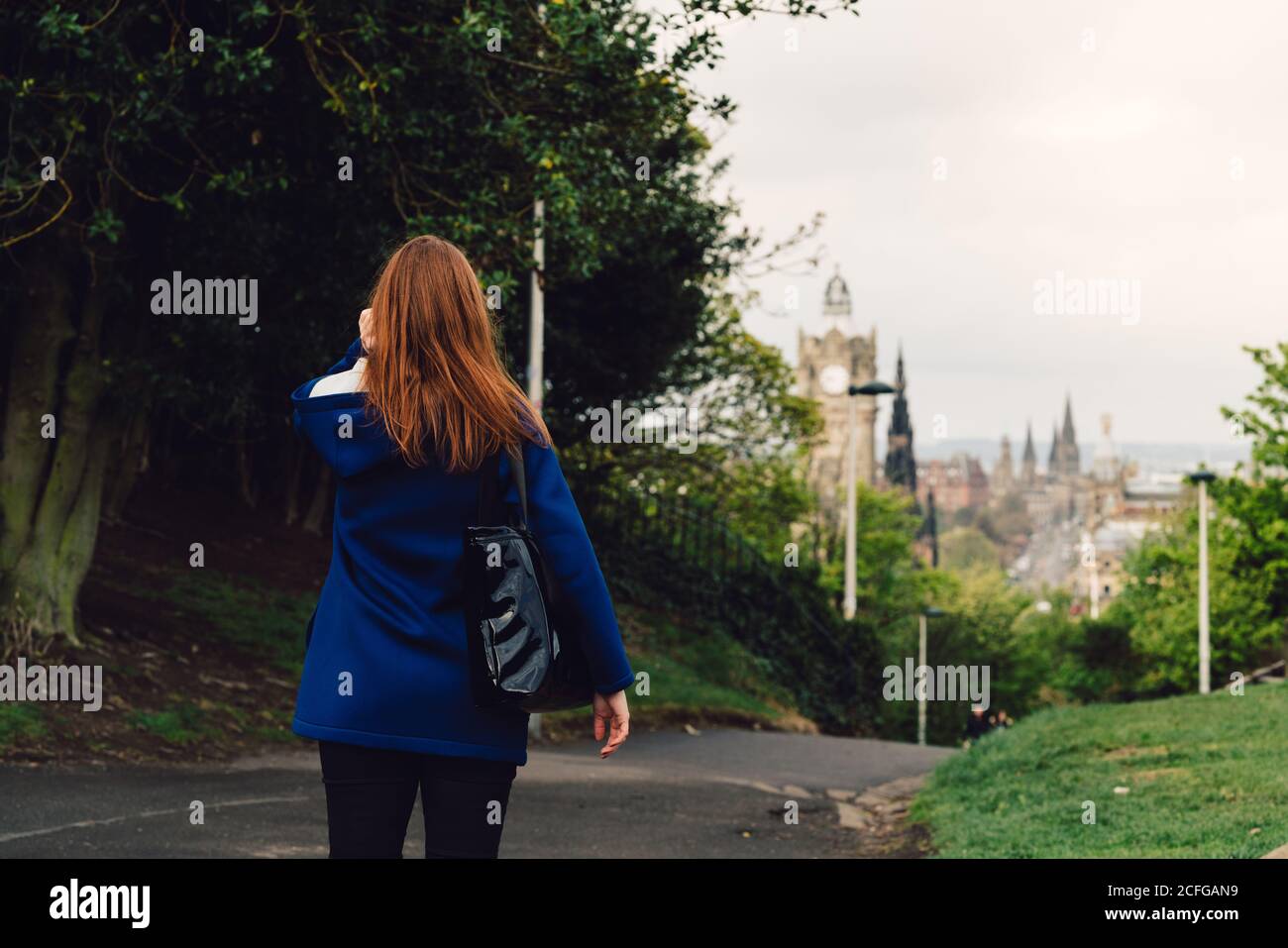 Vue arrière d'une femme méconnue qui marche dans un parc paisible près d'une ville en écosse Banque D'Images