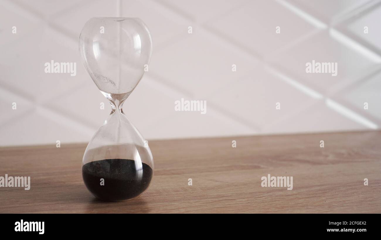 Sablier en cristal avec sable noir sur table en bois et blanc arrière-plan Banque D'Images