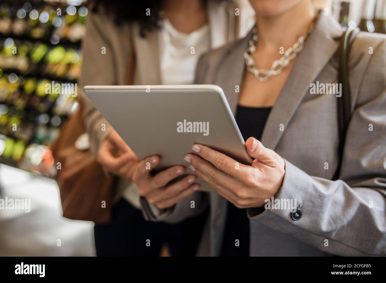 Femme d'affaires sans visage dans une veste grise tenant et parcourant une tablette debout avec un ami. Banque D'Images