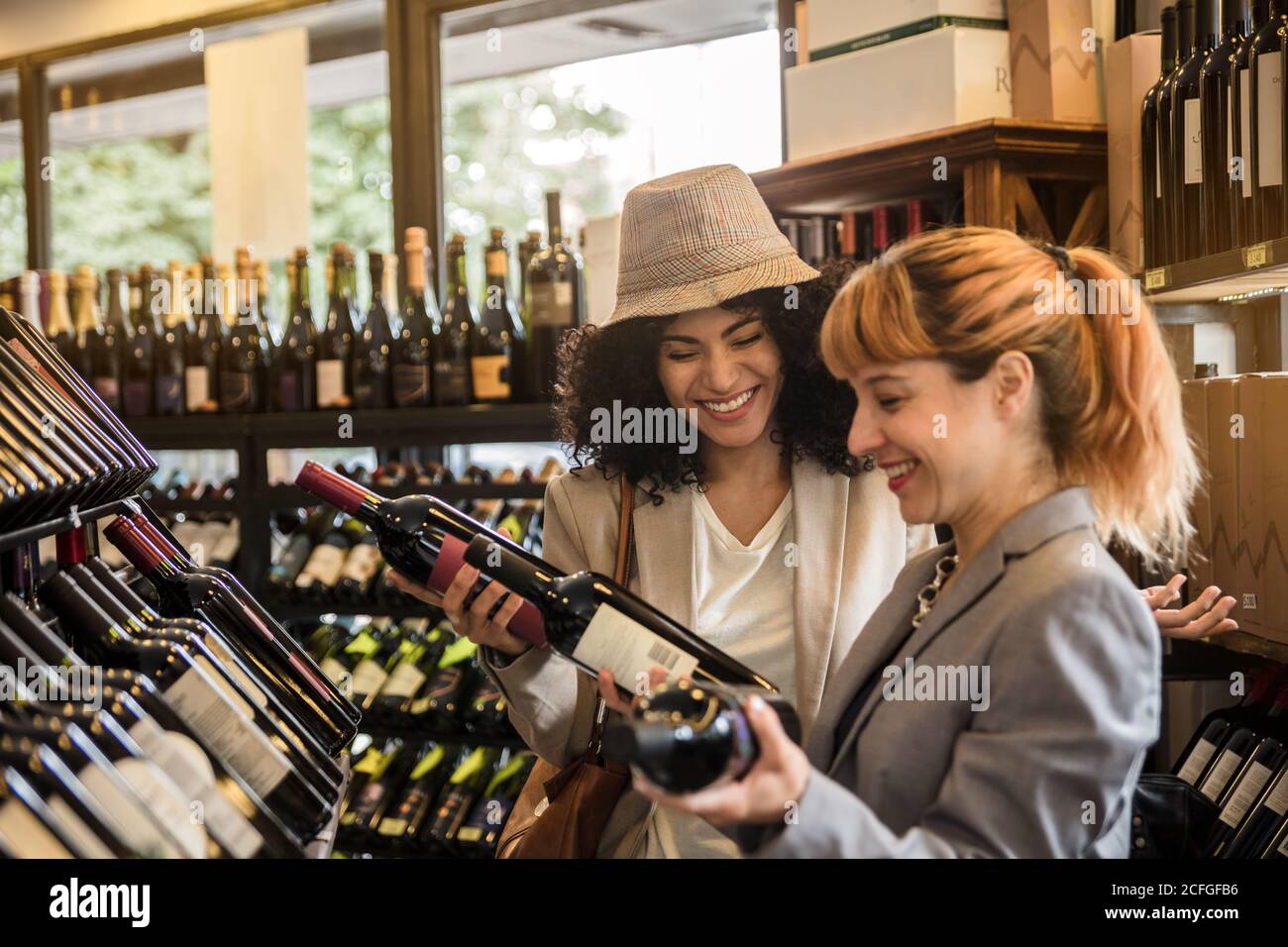 Vue latérale d'une femme joyeuse et variée explorant des étagères de marché du vin avec des bouteilles de vin. Banque D'Images