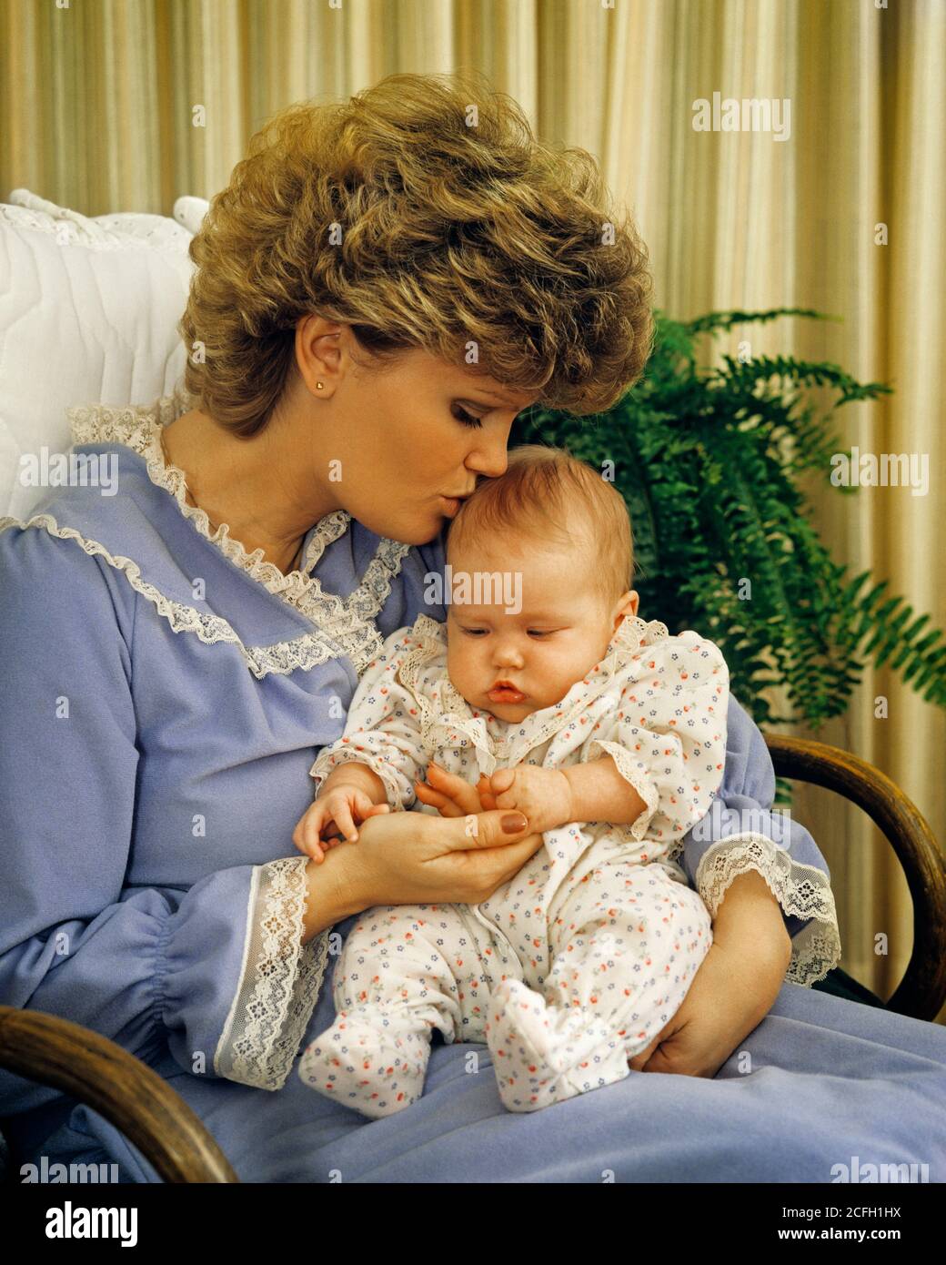 Femme Affectueuse Des Annees 1980 Mere Dans Une Robe De Chambre Assise Dans Un Courbe Chaise Bercante En Bois Tenant Embrassant Nouveau Ne Bebe Fille Fille Kb Tay001 Hars Old Fashion 1