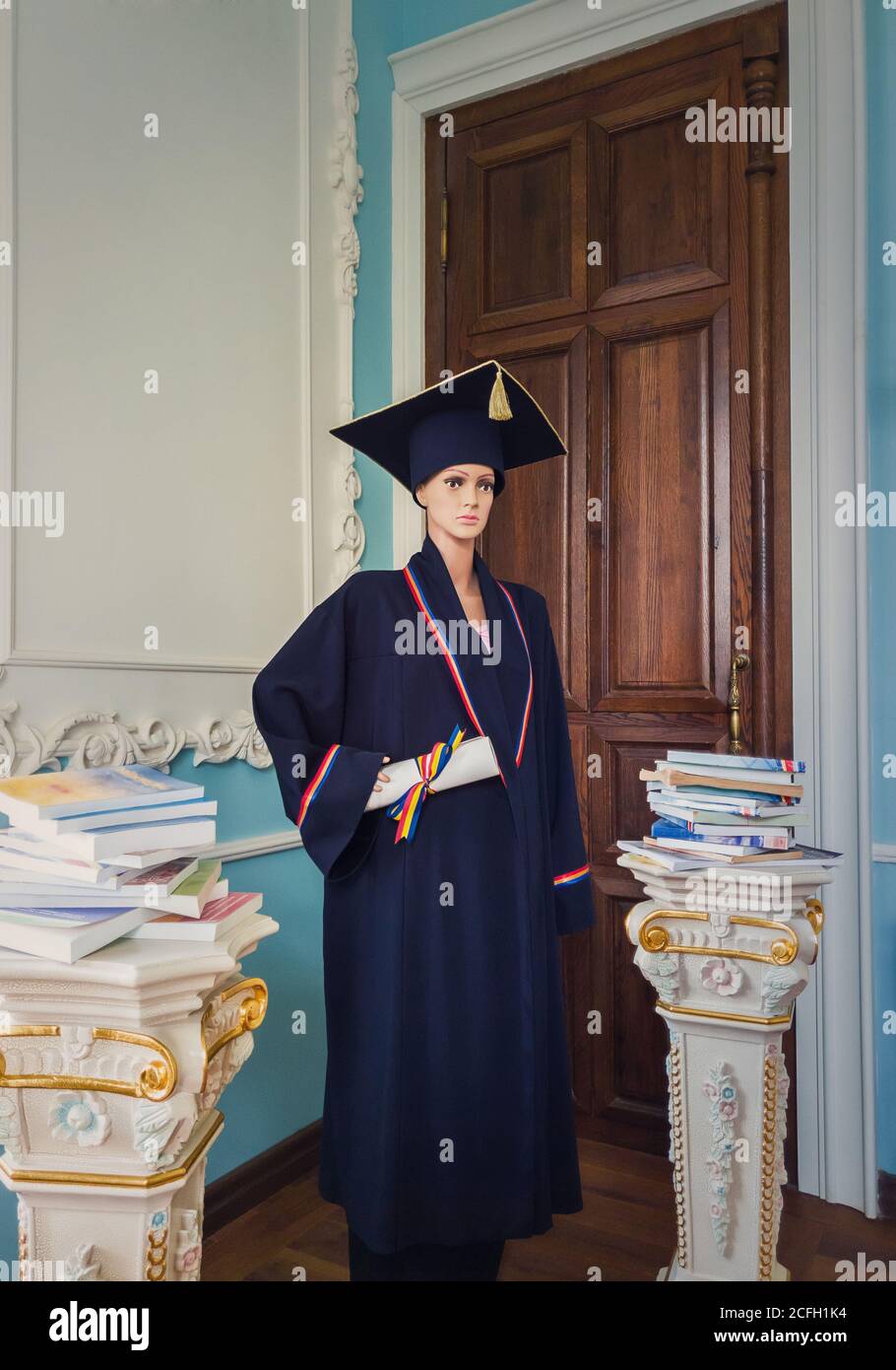 Mannequin étudiant, à l'intérieur d'une bibliothèque, habillé comme un diplômé avec une casquette et une robe noire, tenant un diplôme en main. Beau pil antique orné Banque D'Images
