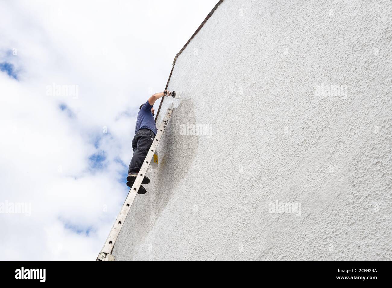 Homme dur haut d'une échelle peint côté de la maison une couleur blanche fraîche. Banque D'Images